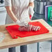 A woman in a white coat and gloves using a red Choice cutting board to cut meat.