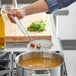 A person using a Choice round mesh skimmer to pour liquid into a pot of soup.