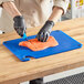 A person in black gloves uses a knife to cut salmon on a blue Choice cutting board.