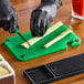 A person cutting celery on a green Choice cutting board on a counter.