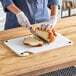 A woman using a Choice white cutting board to cut a loaf of bread.