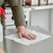 A person wiping a table with a Tork white medium-duty paper wiper.