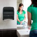 A black electronic touch-free automatic hand towel dispenser mounted on a restroom wall.