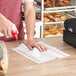 A person using a Tork white and red striped food service wiper to clean a table.