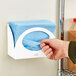 A hand holding a blue plastic Tork wiper dispenser.