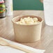 A Choice paper food cup filled with macaroni and cheese on a table.