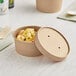 A round Kraft paper food container with a vented lid on a table.