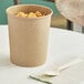 A brown Choice paper food cup filled with rice on a table with a wooden fork.