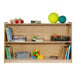 A Flash Furniture wooden classroom storage cabinet with books on the shelves and toys on top.