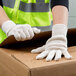 A person wearing Cordova heavy weight natural polyester/cotton work gloves opening a cardboard box.
