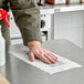 A person cleaning a surface with a white Sani Professional foodservice towel.