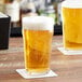 Two glasses of beer on a table, one with foam on top and both on coasters.