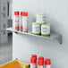 A Lavex stainless steel wall mount shelf with containers and cans on it.