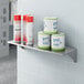 A Lavex stainless steel wall mount shelf with cans on it.
