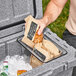 A man putting a bag of bread into a CaterGator clear bin inside a cooler.