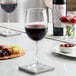 Two Acopa Select Flora wine glasses on a table with a glass of red wine and a bowl of red food.