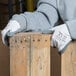 A person wearing Cordova white nylon gloves with gray nitrile palm coating and holding a piece of wood.