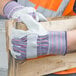 A person wearing Cordova striped canvas work gloves with leather palms and rubber cuffs holding a piece of wood.