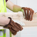 A person wearing Cordova Select Grain Cowhide driver's gloves holding a piece of wood.