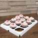 A white tray with Baker's Mark cupcake inserts holding cupcakes with pink frosting and candy on top.
