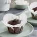 Two chocolate muffins on plates with brown and white Baker's Mark medium rounded muffin wrappers.