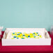 The bottom of a white Baker's Mark full sheet corrugated bakery box with a cake inside decorated with blue and yellow frosting flowers.