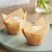Two Baker's Mark unbleached natural Kraft tulip baking cups with cupcakes inside on a plate.