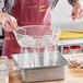 A person using a white Choice breading basket to pour flour into a metal pan.