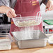 A person pouring flour into a silver metal mesh breading basket.