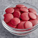 A glass bowl of red Valrhona Raspberry Inspiration chocolate buttons.