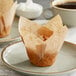 A Baker's Mark unbleached natural kraft tulip baking cup with a cupcake on a plate.