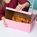 A woman opening a pink Baker's Mark cake box to reveal croissants.