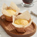 A pair of muffins in large white high crown muffin wraps displayed on a wooden tray.
