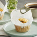 A muffin in a Baker's Mark white medium high crown paper wrapper on a plate next to a cup of coffee.