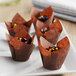 A group of Baker's Mark chocolate brown tulip baking cups on a plate of chocolate cupcakes with colorful sprinkles.