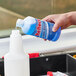 A hand pouring blue Noble Chemical Reflect cleaner from a white bottle into a white plastic container.