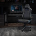 A Flash Furniture black leather high-back gaming chair with 4D armrests in front of a brick wall.