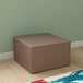 A brown cube ottoman in a corner of a room with wood floors.