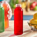 A hand holding a red liquid-filled 16 oz. Round PET Clear HPP Juice Bottle next to a bowl of lemons.