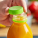 A hand holding a plastic bottle with a lime green tamper-evident cap on it.
