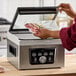 A person using a Galaxy vacuum packaging machine to seal a bag of meat.