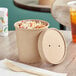 A Choice kraft paper food container with a vented lid on a table full of food.