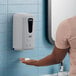 A woman using a Lavex Gray automatic soap dispenser to wash her hands.