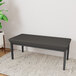 A Lesro Lenox steel bench with black vinyl cushions and a green plant on top.