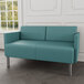 A teal Lesro Luxe Lounge loveseat with upholstered arms and steel legs in a lounge area.