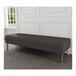 A Lesro Luxe Lounge black vinyl bench with steel legs in a room with a wood floor and white walls.