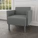 A Lesro Luxe Lounge Series grey guest arm chair with steel legs in a lounge area.