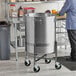 A man standing next to a Vigor stainless steel stock pot dolly in a professional kitchen.