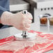 A person wearing gloves uses a Choice stainless steel meat tenderizer.