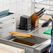 A woman using a Choice 8" round coarse mesh skimmer to fry food in a fryer.